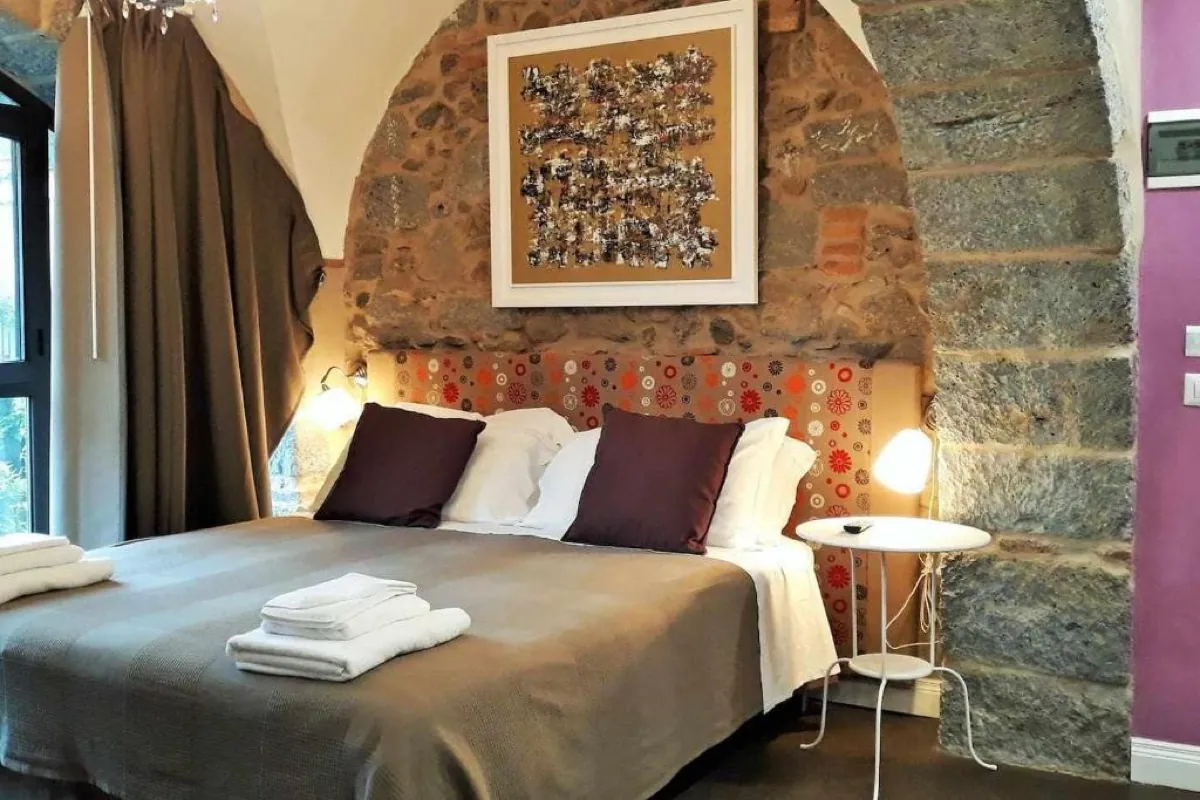 Camera superior con parete color cipria, arco in pietra lavica a vista e letto matrimoniale