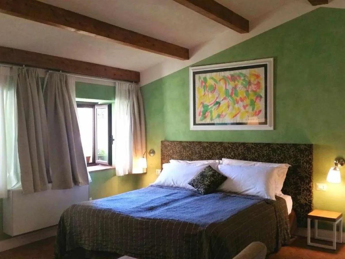 Camera con parete verde, travi in legno e letto matrimoniale con copriletto blu