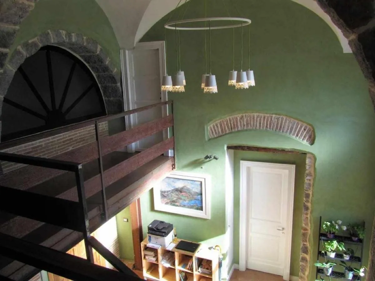 Scala interna con parete verde, archi in pietra lavica e lampadario moderno